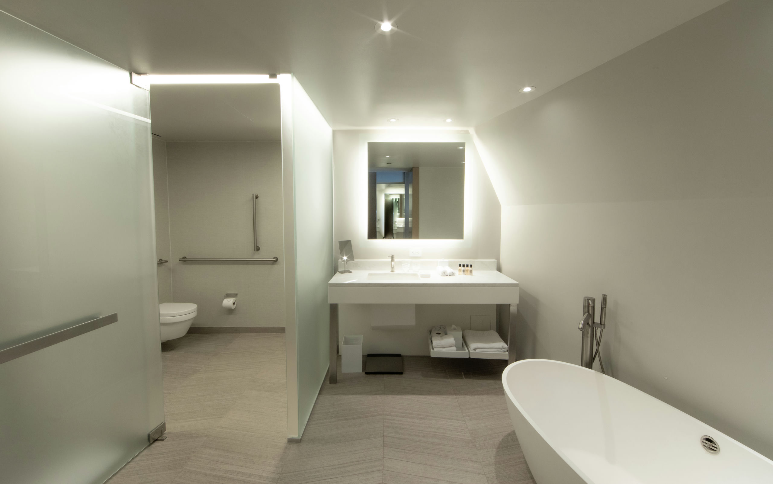 A modern hotel bathroom with a soaking tub, separate shower, floating sink, and tiled floor.