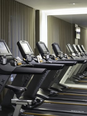 A row of treadmills with TV screens in a gym with a mirrored wall.