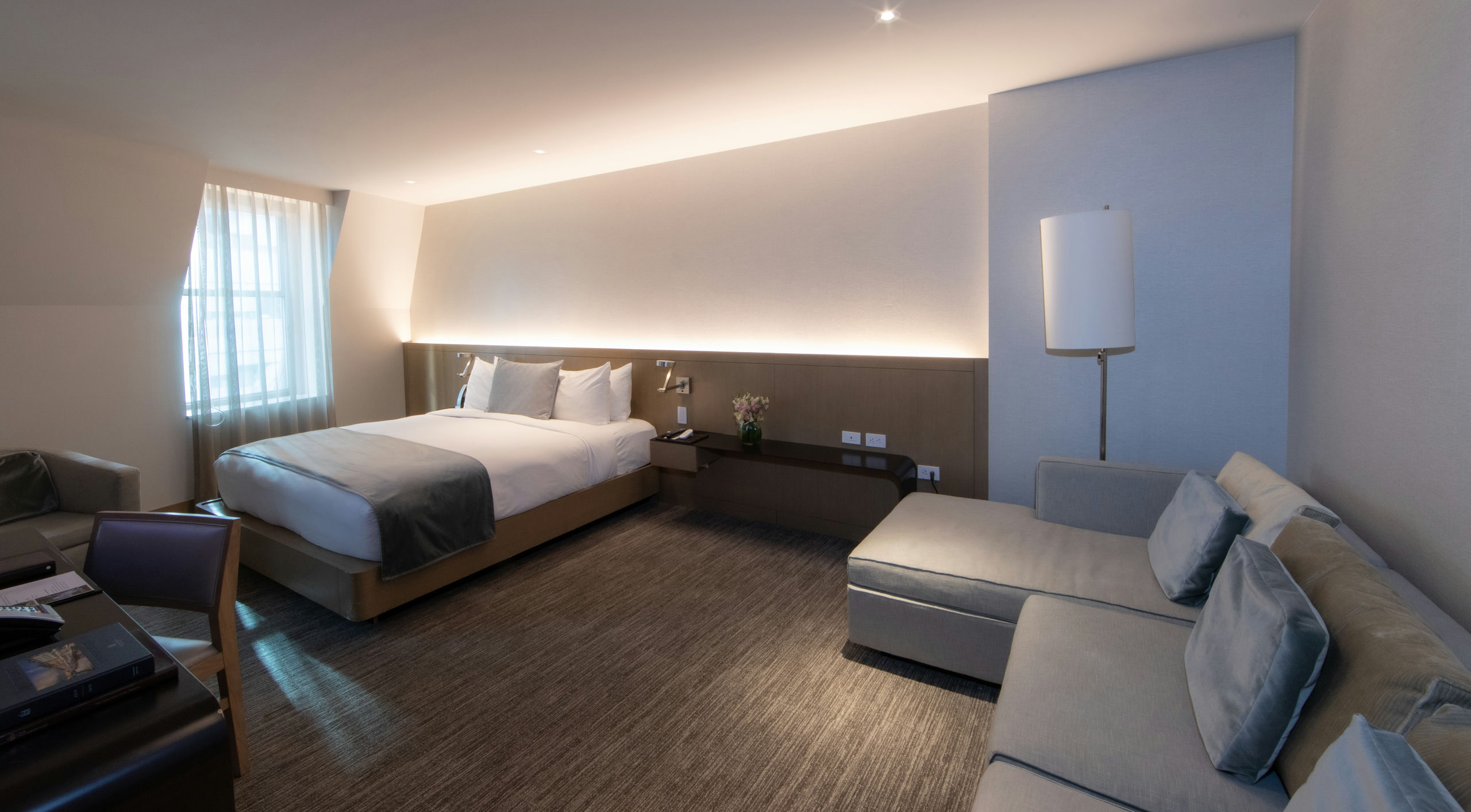 A wide view of a hotel room with a bed, sofa, desk, and lamp.