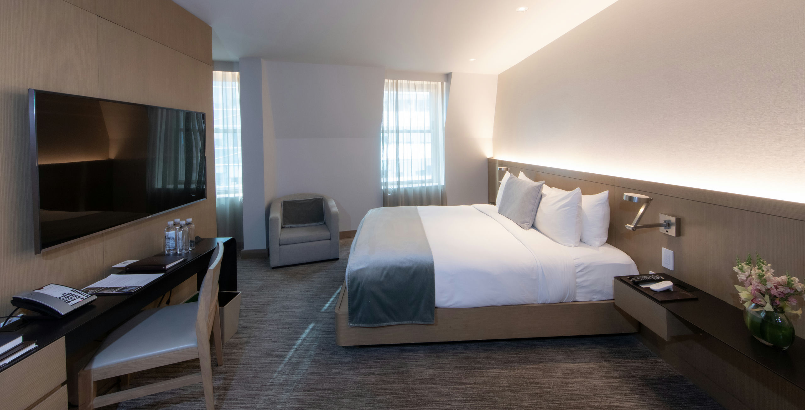 A wide view of a hotel room with a bed, desk, chair, and TV.
