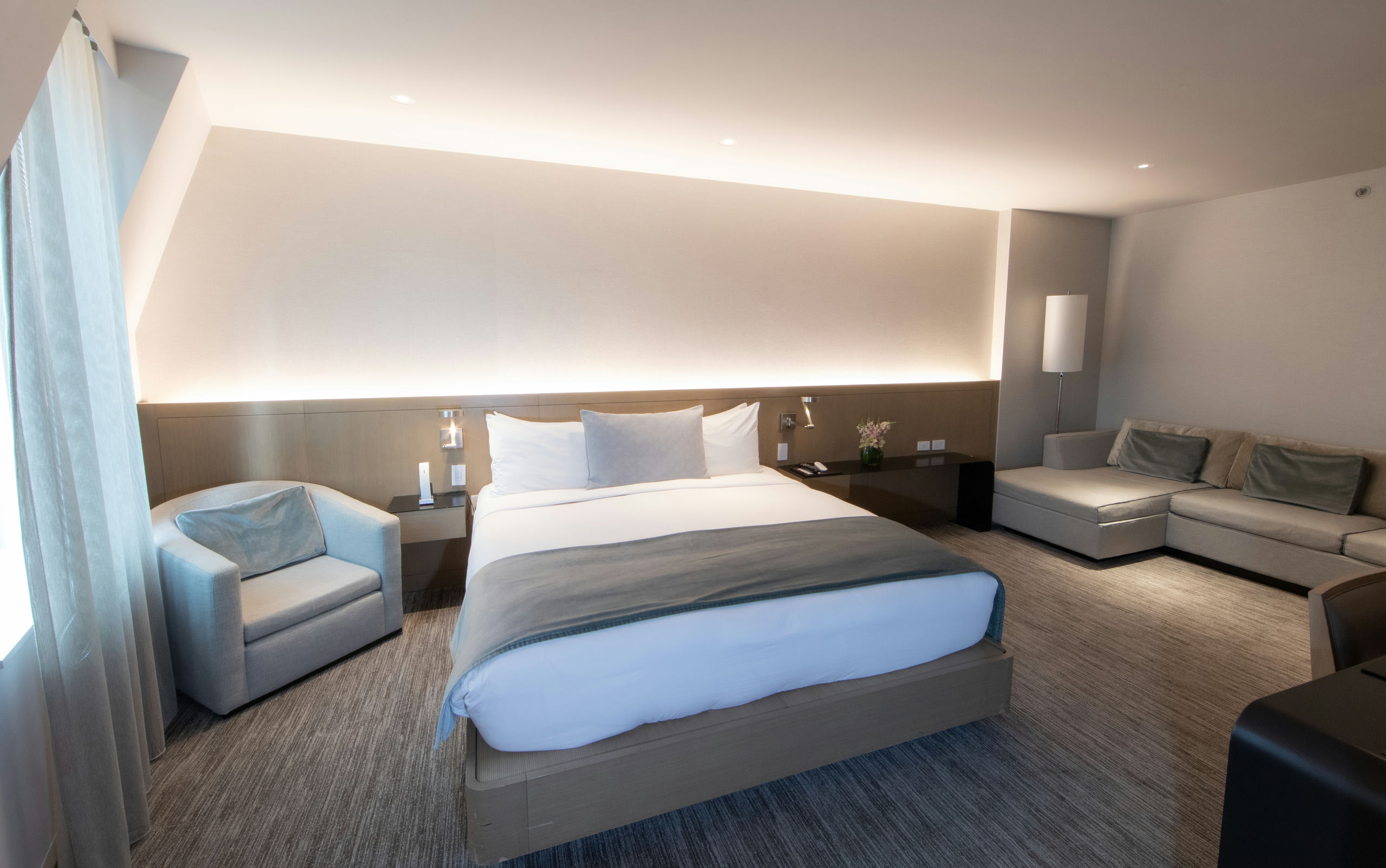 A wide hotel room with a bed, sofa, chair, and nightstand.