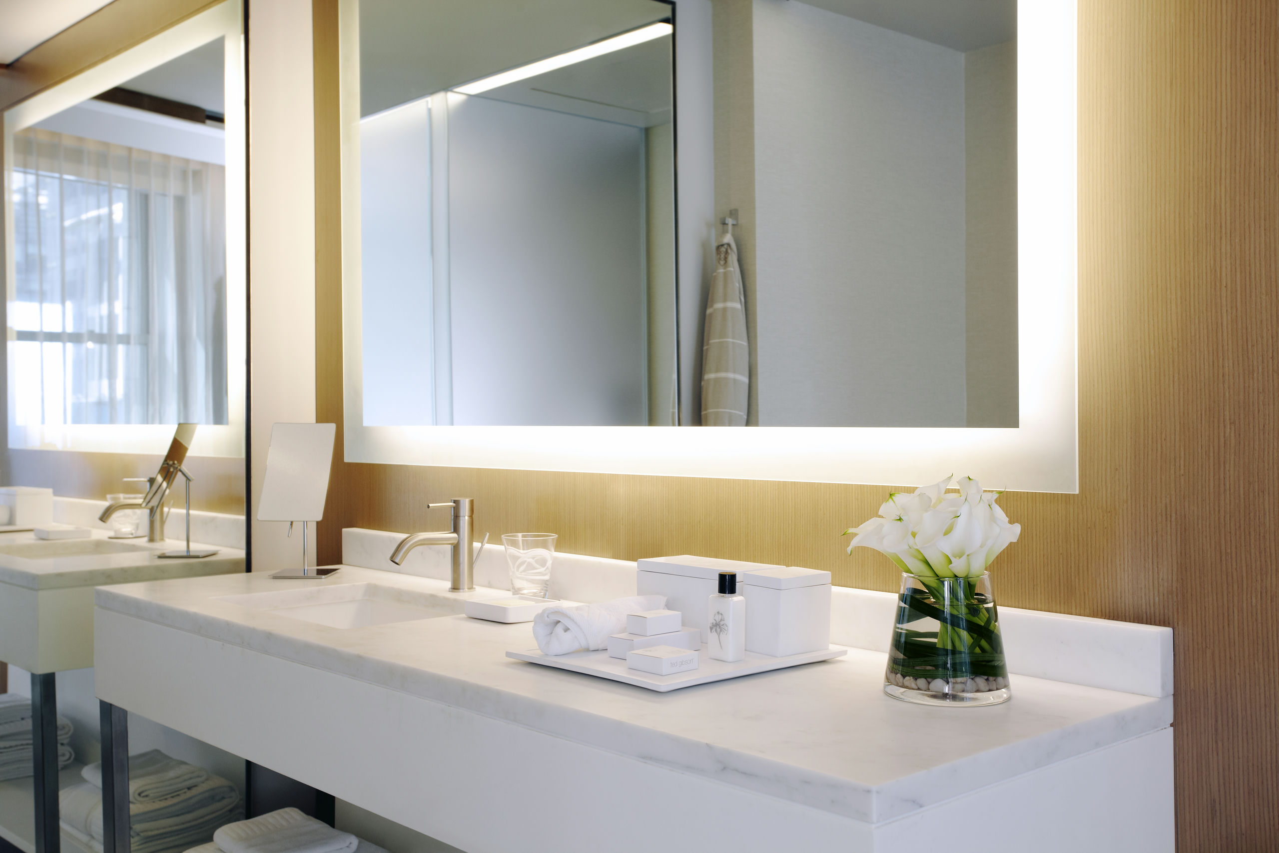 A clean and modern bathroom sink area with a large mirror, marble countertop, and amenities.