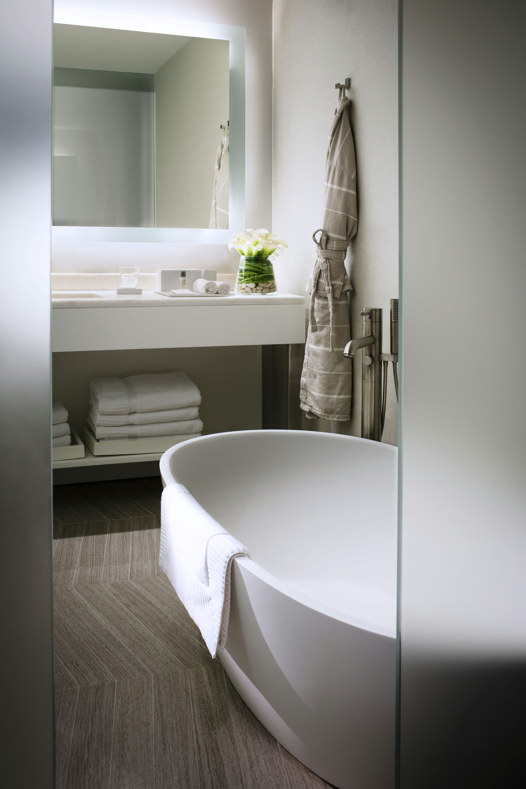 A clean and modern bathroom with a white bathtub, glass shower door, and a sink with towels.