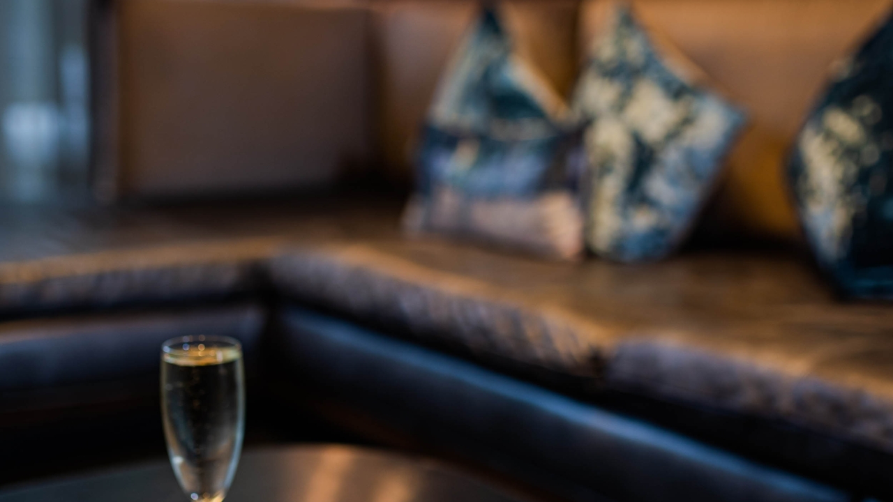 A blurry photo of a champagne flute on a table in front of a couch with pillows.
