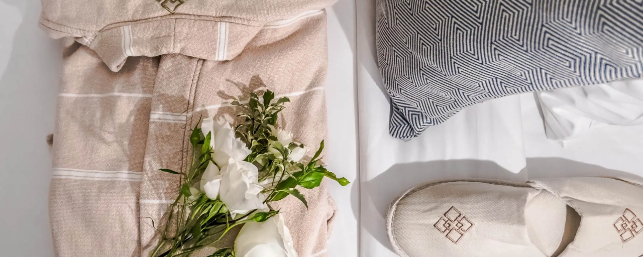 A neatly arranged bed with towels, flowers, and slippers.