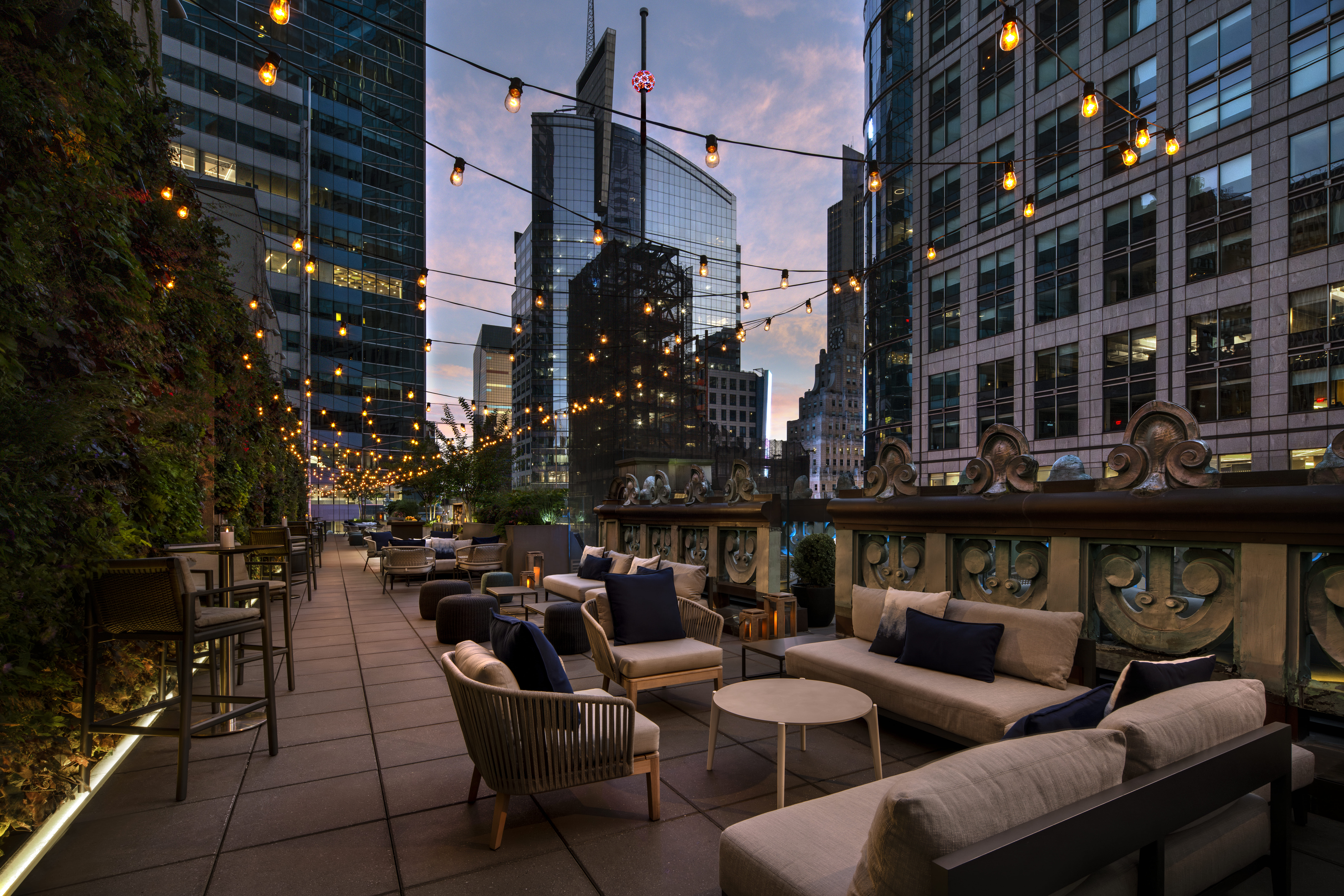 A rooftop lounge with outdoor seating and string lights overlooking the city skyline.