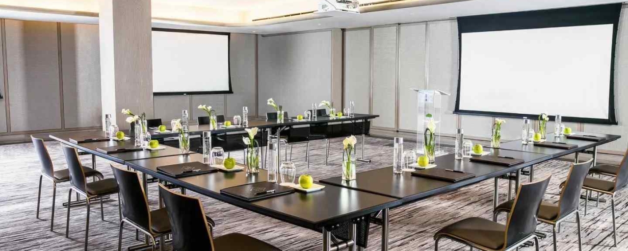 A conference room with long tables, chairs, and projector screens.