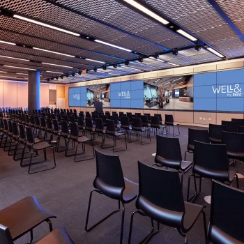 A large meeting room with rows of chairs, tables, and screens on the wall.