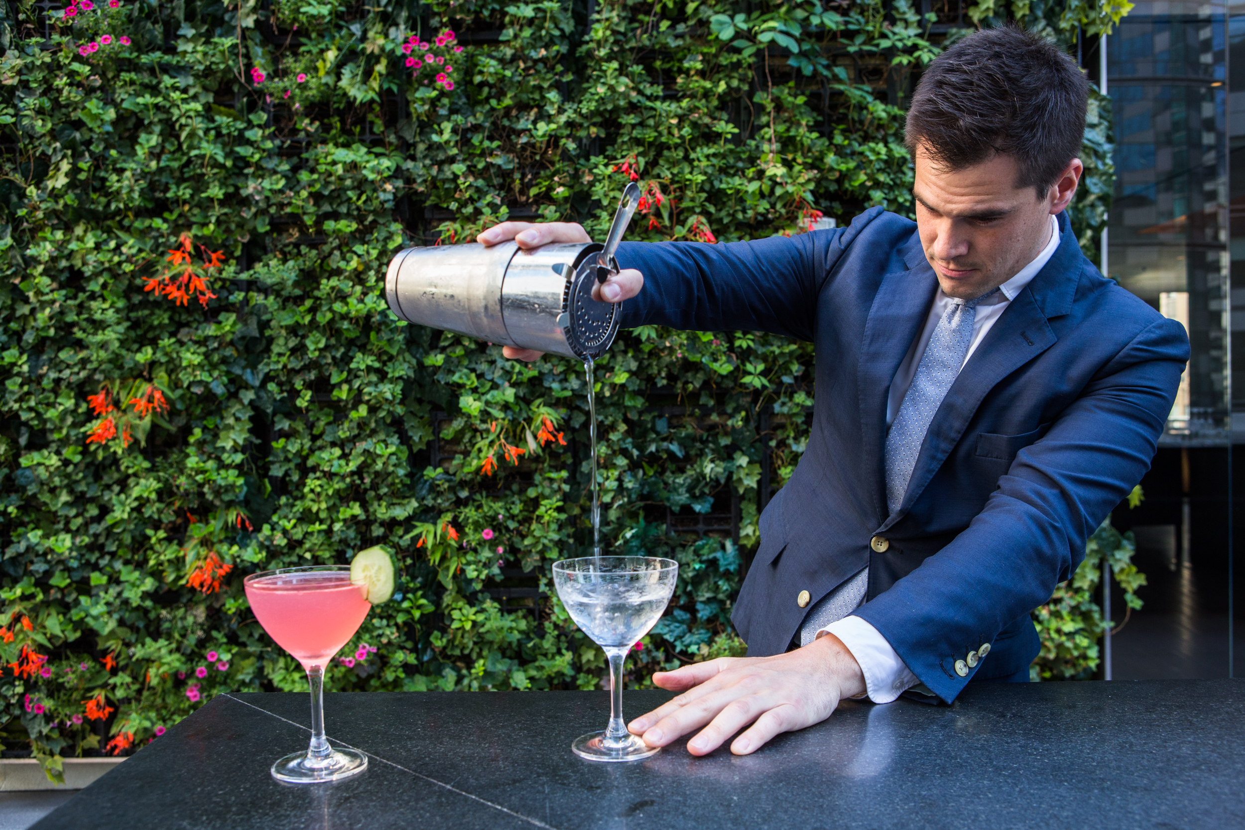 A bartender in a blue suit pouring a drink into a martini glass.